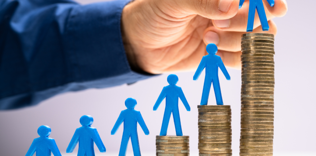 Person putting small blue people figures on stacks of coins